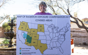 Woman holding map of of the USA with highlighted states that says Map of Radiation Exposure Compensation Act covered area