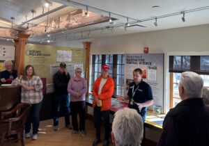 man speaking to group of people at a museum