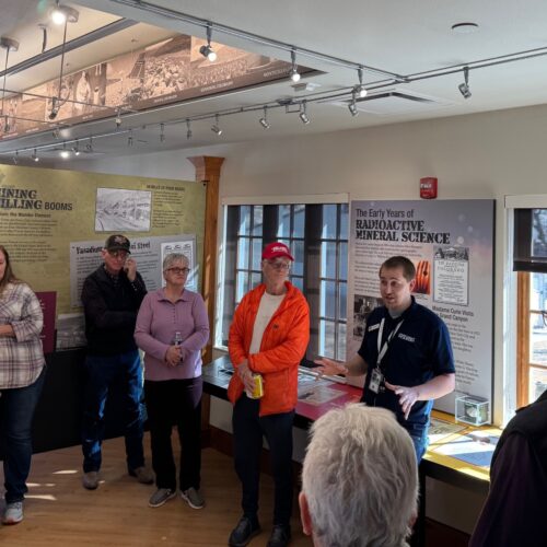 man speaking to group of people at a museum