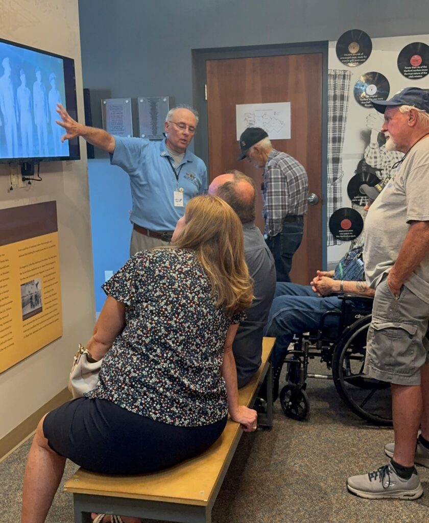 people sitting on a bench while museum tour guide gives presentation
