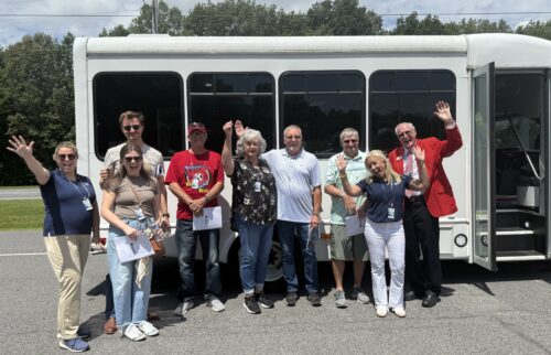 group of people standing in front of a bus, waving