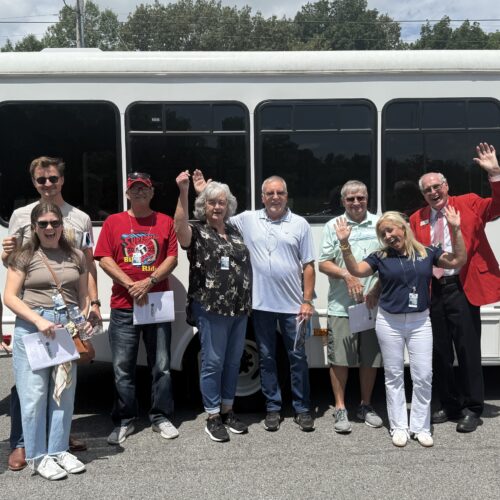 group of people standing in front of a bus, waving