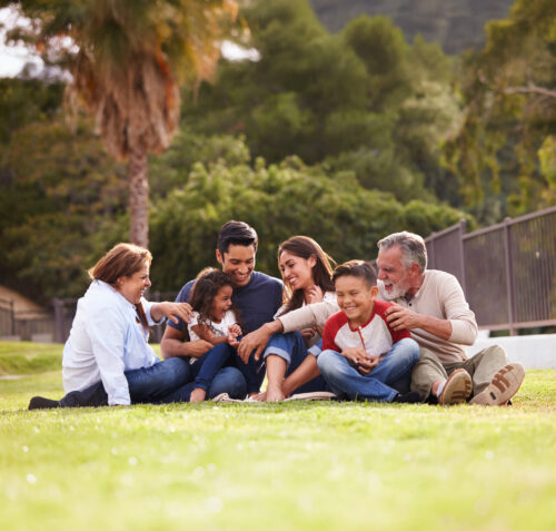 Happy three generation Hispanic family sitting on the grass together in the park, selective focus