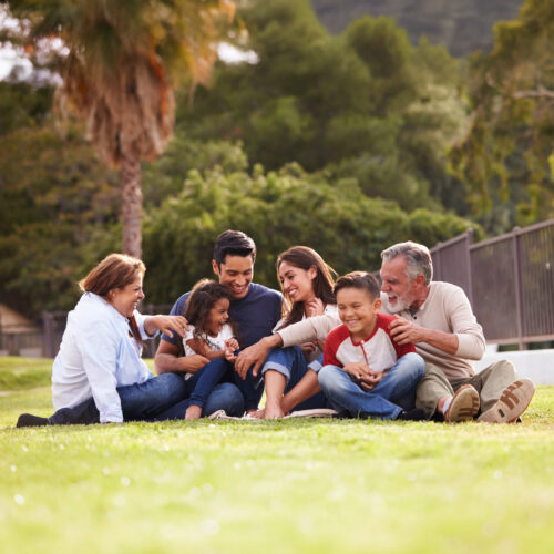 Happy three generation Hispanic family sitting on the grass together in the park, selective focus